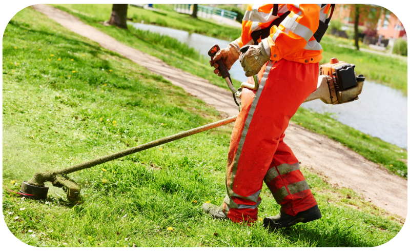 A man in an orange uniform operates a lawn mower, tending to a well-maintained grassy area.